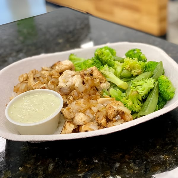 Fit Factory Grill's healthy meal with chicken, onions, broccoli, and snap peas, with a side of dressing.
