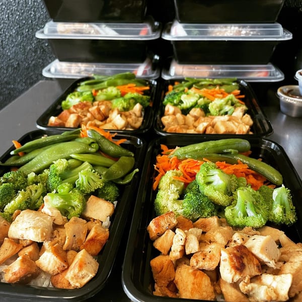 Four Fit Factory Grill meal prep containers filled with chicken, broccoli, carrots, and green beans.