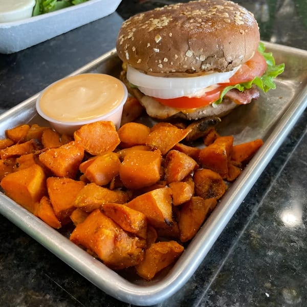 Fit Factory Grill's healthy burger with sweet potato fries and dipping sauce on a metal tray.