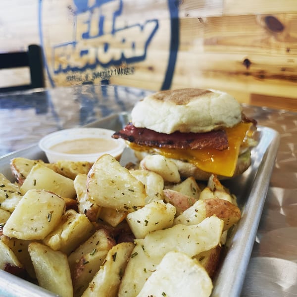 Fit Factory Grill's breakfast sandwich with bacon, egg, and cheese, served with seasoned roasted potatoes.