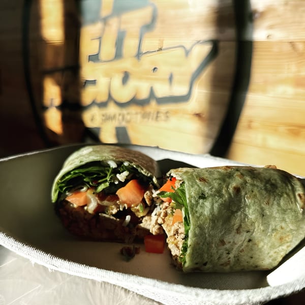 A healthy wrap, cut in half, filled with chicken, rice, lettuce, and tomatoes, on a white tray.
