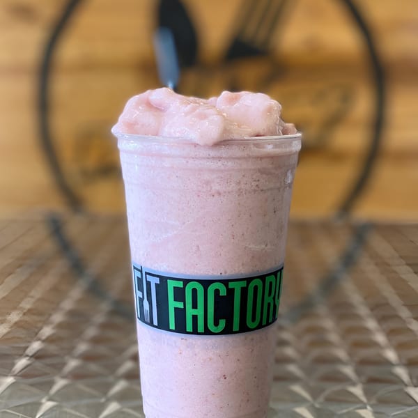 A Fit Factory Grill smoothie, light pink with a thick texture, in a clear cup with a branded label.