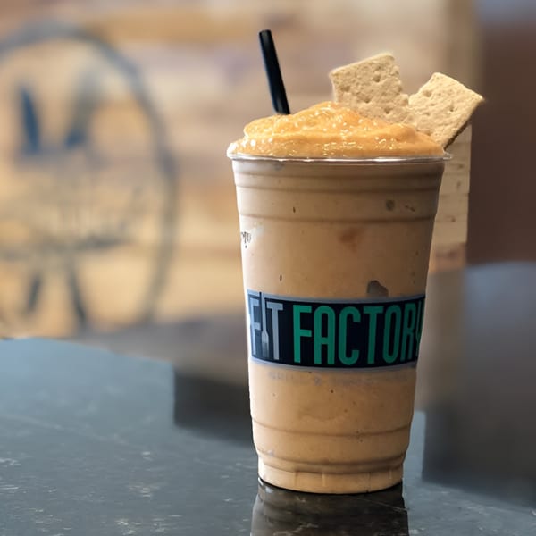 Fit Factory Grill smoothie with a black straw and two graham cracker squares on a dark counter.